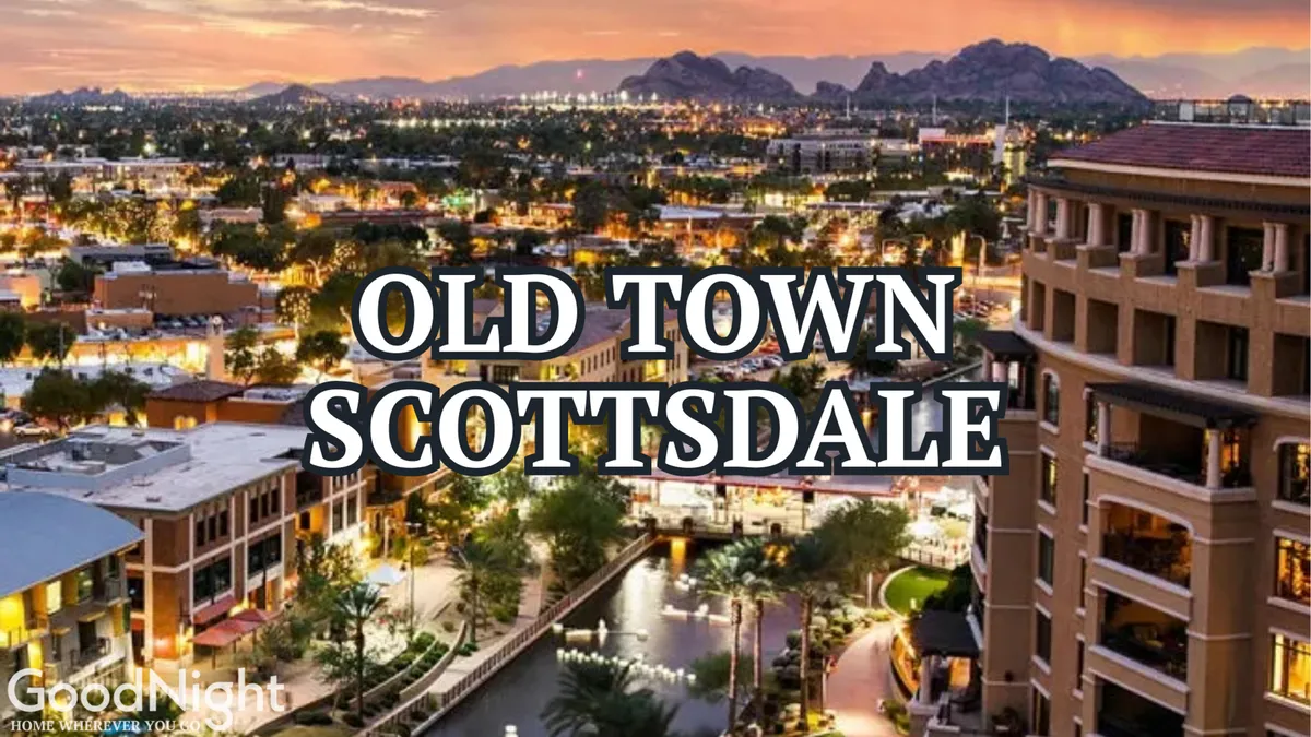 A stunning sunset view over Old Town Scottsdale, with the city's vibrant lights beginning to twinkle. The scene features a waterway lined with palm trees and city buildings, while the distant mountains provide a scenic backdrop. Restaurants, boutique shops, and the lively urban atmosphere are visible, hinting at the dynamic local culture.