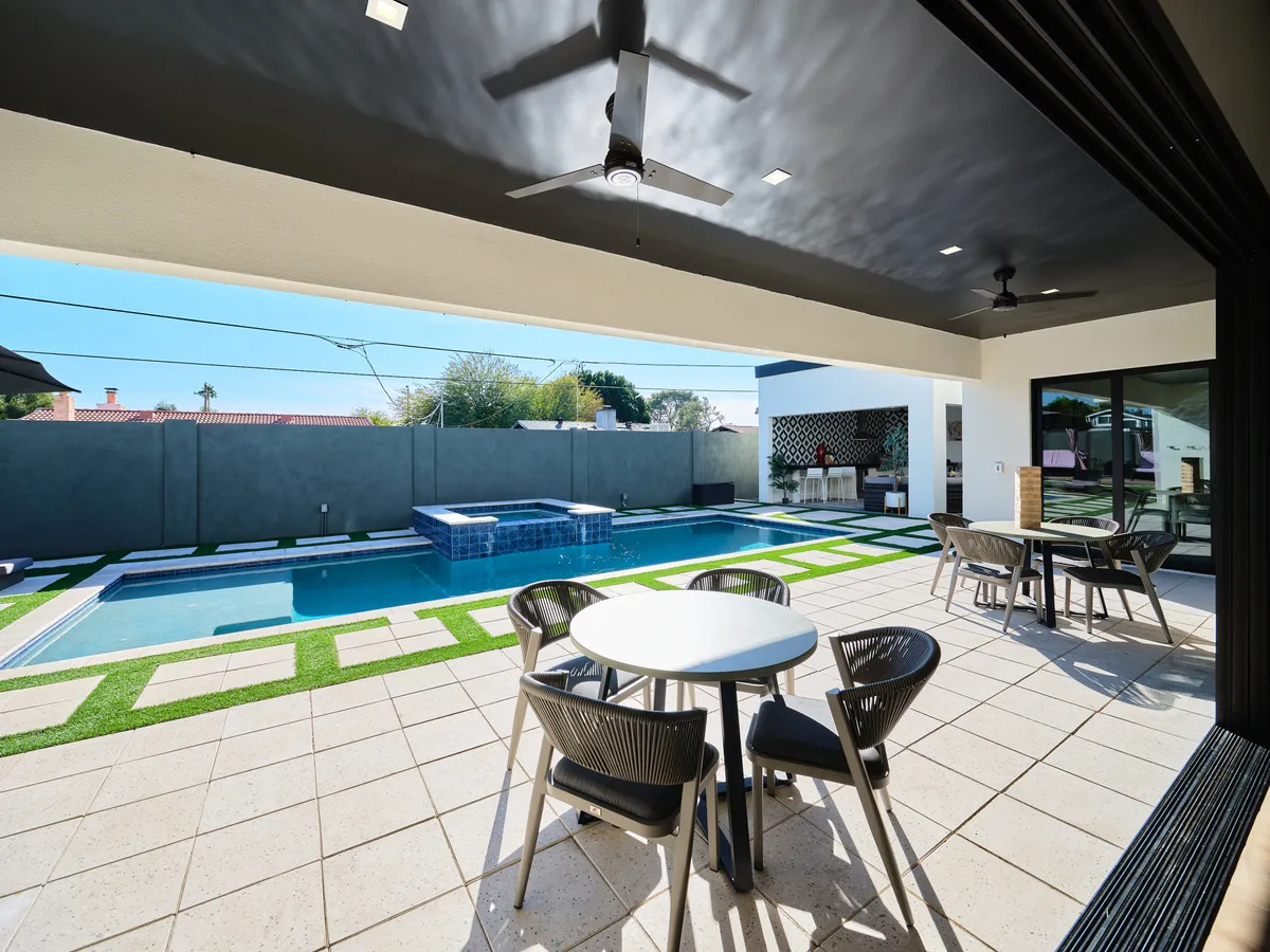 A sparkling swimming pool surrounded by a comfortable outdoor seating area, landscaped grass, and modern architectural features. The sunny, open space suggests a setting ideal for both relaxation and family playtime.