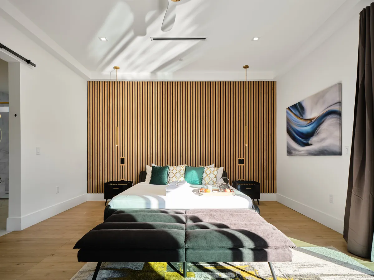A serene bedroom featuring a large bed with textured throw pillows, a wooden accent wall, a unique art piece above the headboard, and soft natural light streaming in, creating an inviting and tranquil atmosphere ideal for rest and relaxation.