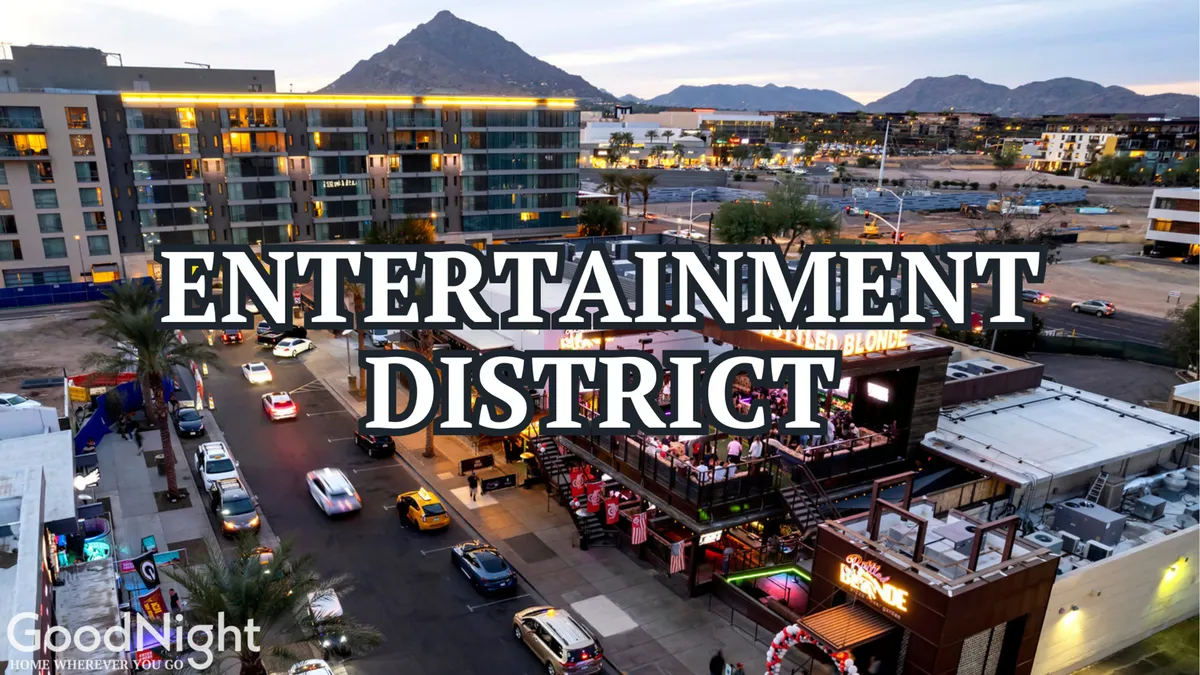 A vibrant exterior street scene of Scottsdale’s Entertainment District at dusk, with illuminated signage, outdoor dining patios, and people gathering. The surrounding mountains are visible in the background, adding a sense of local flair and nighttime excitement.