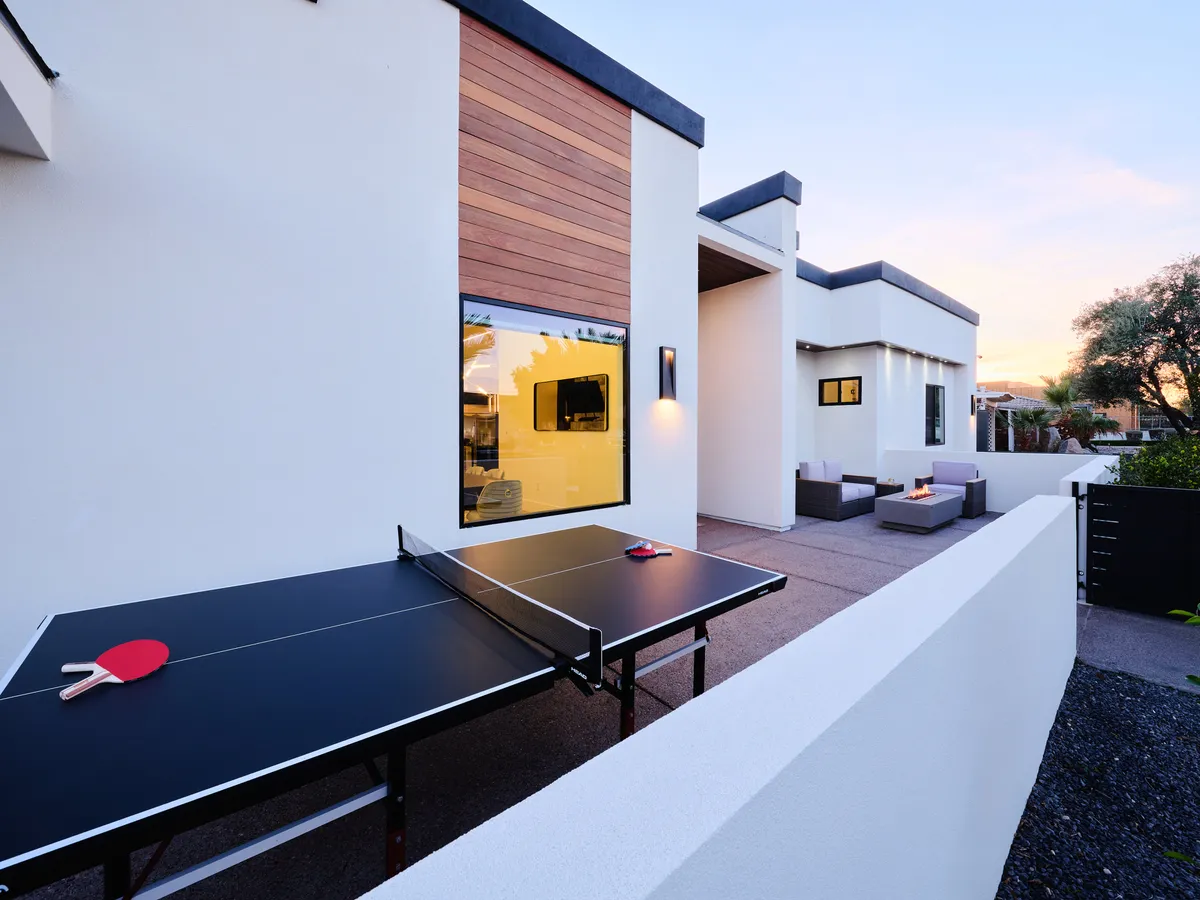 A sleek outdoor setting featuring a modern ping pong table, stylish lounge area, and architectural elements like large windows. The space is designed for both leisure and playful socializing, with ample room for activities and gatherings.