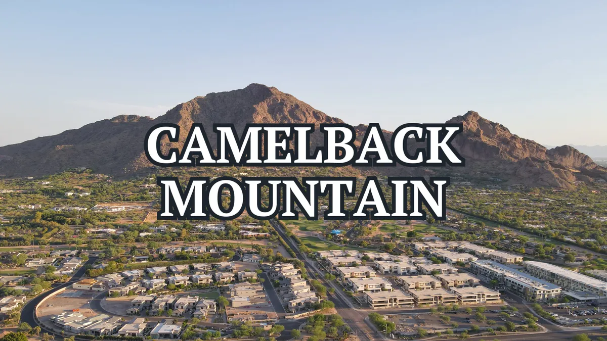 An expansive view of Camelback Mountain rising above lush residential areas and green park spaces, all bathed in clear desert light. The landscape invites outdoor adventure and exploration.
