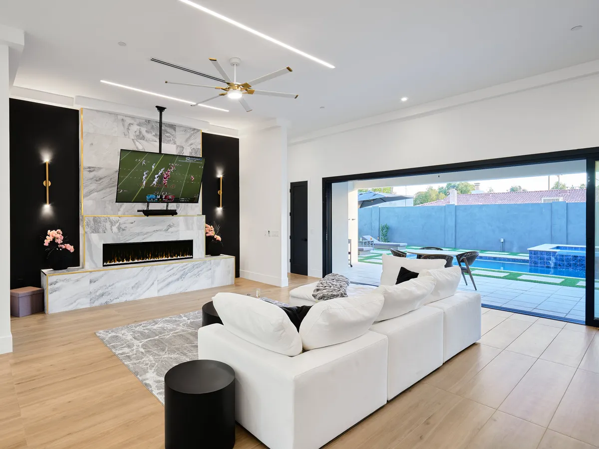A modern living space centered around a marble fireplace, large TV, contemporary sofa, and open sliding doors leading to the pool. The room feels relaxed yet sophisticated, ideal for both family time and personal relaxation.