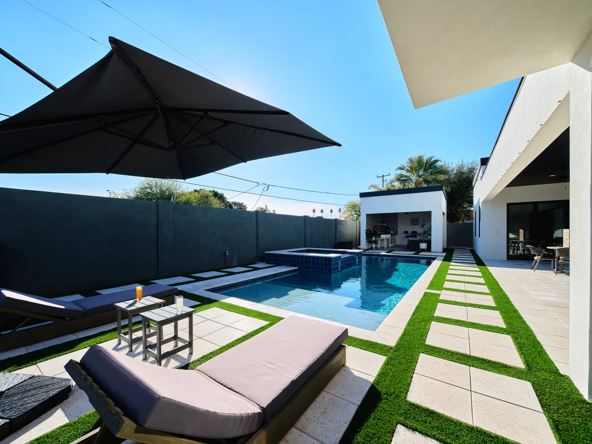 A serene exterior scene featuring a sparkling swimming pool surrounded by lounge chairs, an outdoor dining area, and an umbrella—inviting relaxation and socializing.